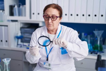 Téléchargez les photos : Femme scientifique senior utilisant une loupe tenant la pilule au laboratoire - en image libre de droit