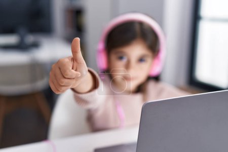 Photo for Adorable hispanic girl student using laptop and headphones doing ok gesture at classroom - Royalty Free Image