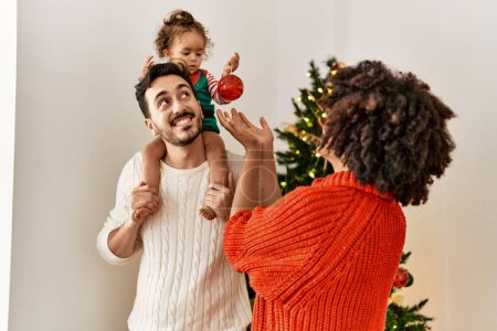 Foto de Pareja e hija sonriendo confiadas decorando el árbol de Navidad en casa - Imagen libre de derechos