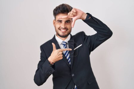 Foto de Young hispanic man with tattoos wearing business suit and tie smiling making frame with hands and fingers with happy face. creativity and photography concept. - Imagen libre de derechos