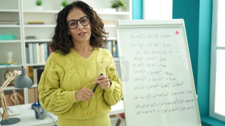 Photo for Middle age hispanic woman teacher explaining maths exercise at library university - Royalty Free Image