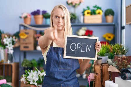 Téléchargez les photos : Young caucasian woman working at florist with open sign pointing with finger to the camera and to you, confident gesture looking serious - en image libre de droit