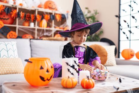 Foto de Adorable chica hispana con disfraz de halloween sosteniendo dulces en casa - Imagen libre de derechos