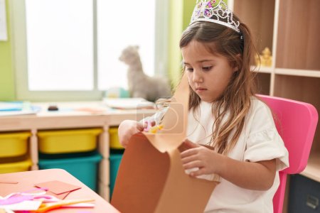 Téléchargez les photos : Adorable étudiante blonde portant le papier de coupe de la couronne de princesse à la maternelle - en image libre de droit