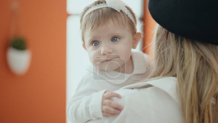 Téléchargez les photos : Adorable bébé blonde souriant confiant sur les bras de la mère à la maison - en image libre de droit