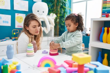 Photo for Teacher and toddler playing with toys sitting on table at kindergarten - Royalty Free Image