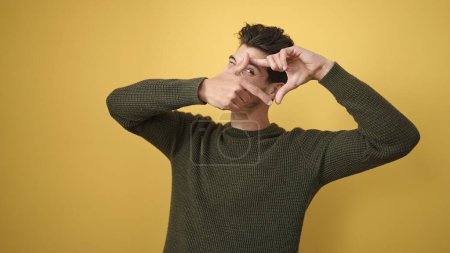 Foto de Joven hombre hispano sonriendo confiado haciendo gesto fotográfico con las manos sobre el aislado fondo amarillo - Imagen libre de derechos