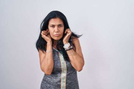 Téléchargez les photos : Mature hispanic woman standing over white background covering ears with fingers with annoyed expression for the noise of loud music. deaf concept. - en image libre de droit