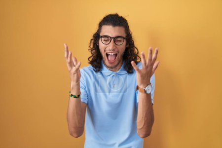 Photo for Young hispanic man standing over yellow background celebrating mad and crazy for success with arms raised and closed eyes screaming excited. winner concept - Royalty Free Image
