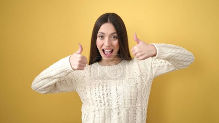 Téléchargez les photos : Jeune belle femme hispanique souriant confiant faire ok signe avec les pouces vers le haut sur fond jaune isolé - en image libre de droit