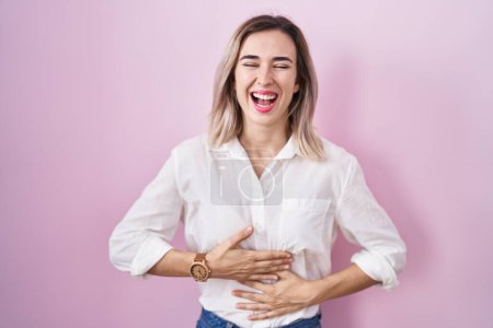 Foto de Young beautiful woman standing over pink background smiling and laughing hard out loud because funny crazy joke with hands on body. - Imagen libre de derechos
