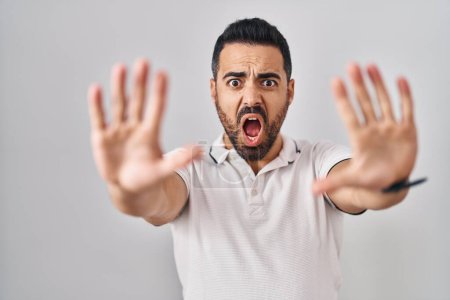 Foto de Young hispanic man with beard wearing casual clothes over white background doing stop gesture with hands palms, angry and frustration expression - Imagen libre de derechos