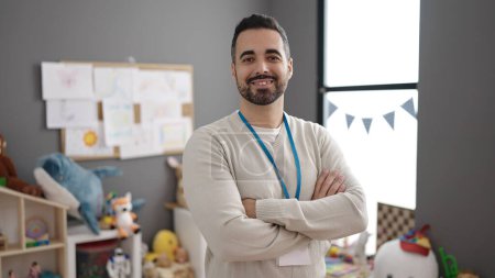 Photo for Young hispanic man teacher smiling confident standing with arms crossed gesture at kindergarten - Royalty Free Image