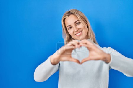 Photo for Young caucasian woman standing over blue background smiling in love doing heart symbol shape with hands. romantic concept. - Royalty Free Image