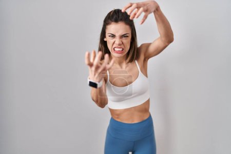 Foto de Mujer hispana usando ropa deportiva sobre fondo aislado gritando frustrada con rabia, manos tratando de estrangular, gritando loco - Imagen libre de derechos