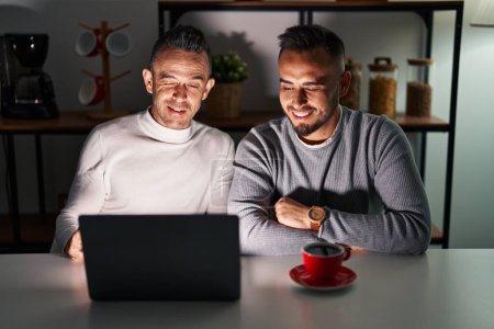Téléchargez les photos : Couple homosexuel en utilisant ordinateur portable clin d'oeil en regardant la caméra avec une expression sexy, gai et heureux visage. - en image libre de droit