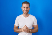 Young caucasian man standing over blue background hands together and fingers crossed smiling relaxed and cheerful. success and optimistic  Tank Top #640430178