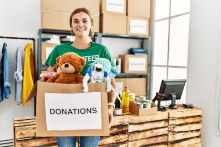 Téléchargez les photos : Jeune femme portant un uniforme bénévole tenant un paquet de dons de jouets au centre de bienfaisance - en image libre de droit