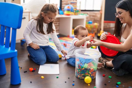 Photo for Teacher with boy and girl playing with construction blocks sitting on floor at kindergarten - Royalty Free Image
