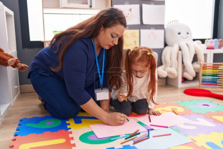 Photo for Teacher and student drawing on paper sitting on floor at kindergarten - Royalty Free Image