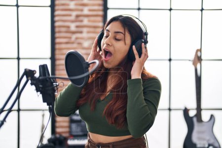 Foto de Joven mujer hispana músico cantando canción en estudio de música - Imagen libre de derechos
