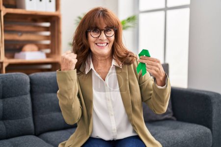 Photo for Middle age hispanic woman holding support green ribbon screaming proud, celebrating victory and success very excited with raised arms - Royalty Free Image