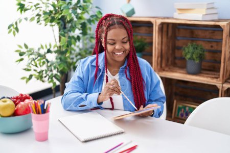 Téléchargez les photos : Femme artiste afro-américaine souriant dessin confiant sur ordinateur portable à la maison - en image libre de droit