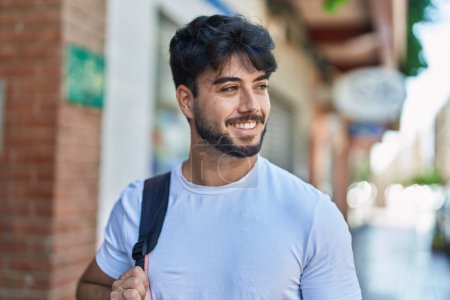 Téléchargez les photos : Jeune homme hispanique souriant confiant portant un sac à dos dans la rue - en image libre de droit