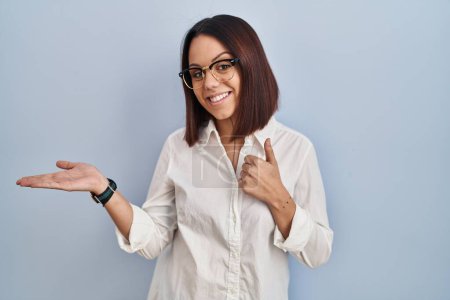 Foto de Young hispanic woman standing over white background showing palm hand and doing ok gesture with thumbs up, smiling happy and cheerful - Imagen libre de derechos