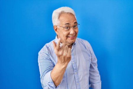 Foto de Hombre mayor hispano con gafas haciendo señas ven aquí gesto con la mano invitando a la bienvenida feliz y sonriente - Imagen libre de derechos