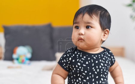 Téléchargez les photos : Adorable bébé hispanique assis sur le lit dans la chambre - en image libre de droit