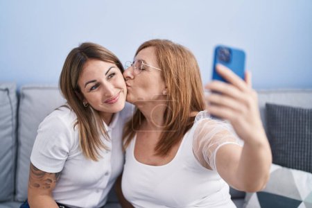 Foto de Mother and daughter making selfie by the smartphone sitting on sofa at home - Imagen libre de derechos