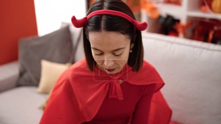 Téléchargez les photos : Young beautiful hispanic woman wearing devil costume sitting on sofa at street - en image libre de droit
