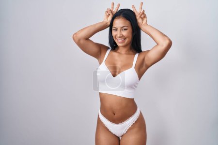 Foto de Hispanic woman wearing lingerie posing funny and crazy with fingers on head as bunny ears, smiling cheerful - Imagen libre de derechos