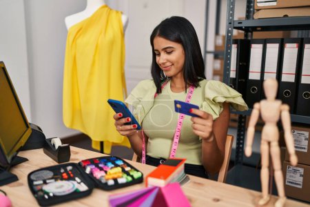 Foto de Trabajadora de negocios de comercio electrónico de mujer latina joven usando teléfono inteligente y tarjeta de crédito en el estudio de diseño - Imagen libre de derechos