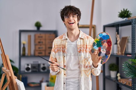 Téléchargez les photos : Young hispanic man artist holding paintbrush and palette at art studio - en image libre de droit