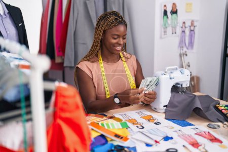 Téléchargez les photos : Femme afro-américaine tailleur souriant confiant compter les dollars au magasin de tailleur - en image libre de droit