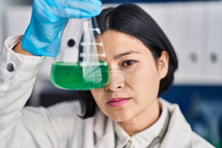 Photo for Young chinese woman scientist holding test tube over eye at laboratory - Royalty Free Image