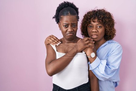 Foto de Dos mujeres africanas de pie sobre fondo rosa expresión despistada y confusa. concepto de duda. - Imagen libre de derechos