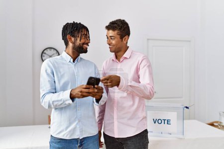 Téléchargez les photos : Deux hommes souriants confiants en utilisant un smartphone au collège électoral - en image libre de droit
