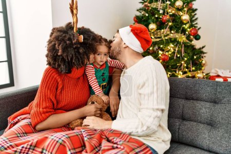 Foto de Pareja e hija besando a un niño sentado junto al árbol de Navidad en casa - Imagen libre de derechos