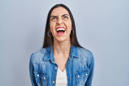 Téléchargez les photos : Femme hispanique debout sur fond bleu en colère et fou hurlant frustré et furieux, criant de colère. rage et concept agressif. - en image libre de droit