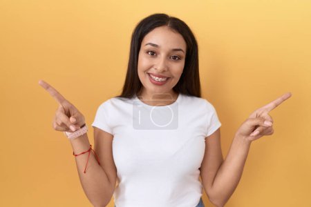 Téléchargez les photos : Young arab woman wearing casual white t shirt over yellow background smiling confident pointing with fingers to different directions. copy space for advertisement - en image libre de droit
