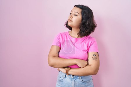 Téléchargez les photos : Jeune femme hispanique debout sur fond rose regardant du côté avec les bras croisés convaincus et confiants - en image libre de droit