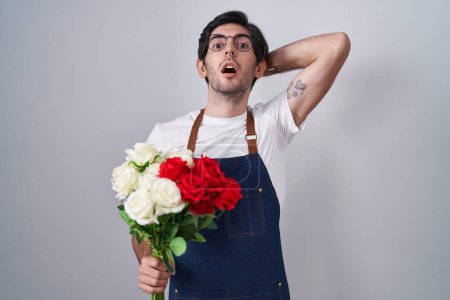 Foto de Young hispanic man holding bouquet of white and red roses crazy and scared with hands on head, afraid and surprised of shock with open mouth - Imagen libre de derechos