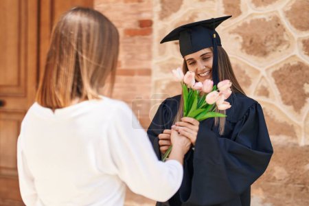 Photo for Two women mother and graduated daughter holding flowers at campus university - Royalty Free Image