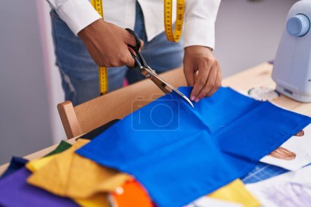 Photo for Young hispanic teenager tailor cutting cloth at tailor shop - Royalty Free Image