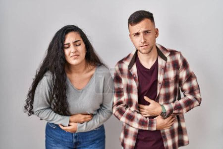Photo for Young hispanic couple standing over white background with hand on stomach because indigestion, painful illness feeling unwell. ache concept. - Royalty Free Image