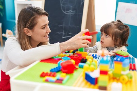 Foto de Profesor y niño pequeño jugando con bloques de construcción sentados en la mesa en el jardín de infantes - Imagen libre de derechos