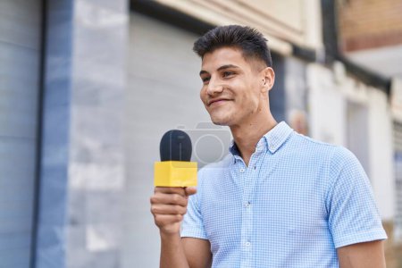Téléchargez les photos : Young hispanic man reporter working using microphone at street - en image libre de droit